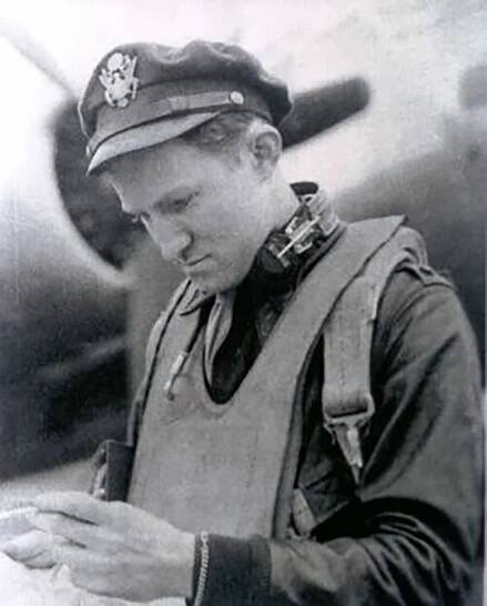 MAJOR H. H. CROSBY (Anthony Boyle). A black and white photo depicting a man in an army shirt with tie and army hat looking at his hands. An uninflated life jacket hangs around his neck.