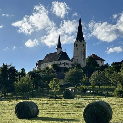 Die Umgebung des Bauernhofs mit einer Kirche auf einem Hügel und Heuballen auf der Wiese.