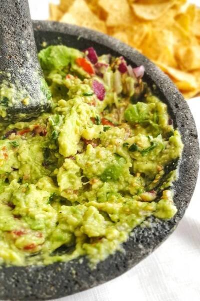 Guacamole in a molcajete surrounded by tortilla chips and ingredients.