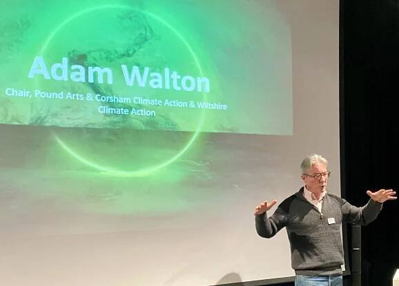 Adam Walton stands infrom of a projector screen that reads "Adam Walton, Chair, Pound Arts & Corsham Climate Action & Wiltshire Climate Action