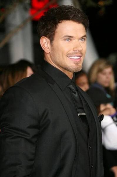 a man in a black suit and tie standing on a red carpet at an event