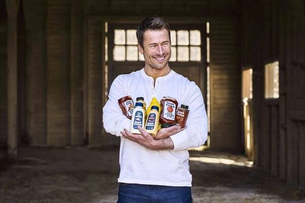 Glen Powell with several bottles of Smash Kitchen products. 