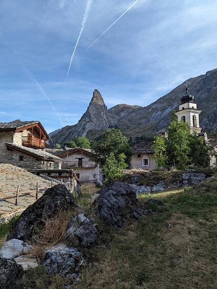Das kleine Dorf Chiappera liegt idyllisch vor einer dramatischen Felsformation. Eine Kirche mit markantem Turm und traditionelle Steinhäuser prägen das Ortsbild. 