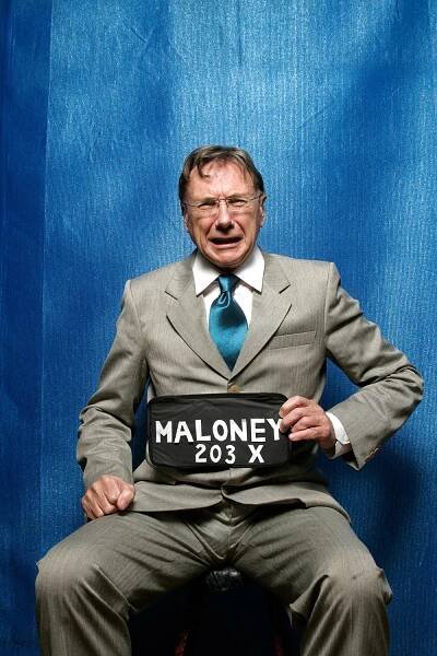 Shane Maloney In Suit Holding Name Tag With Blue Backdrop Portrait