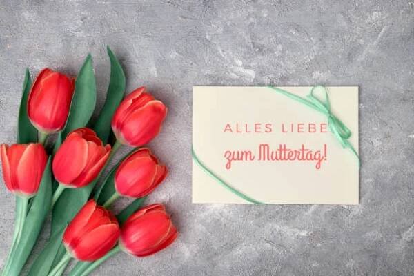 "alles liebe zum muttertag", to znamená v němčině "veškerá láska na den matek". text na papírové kartě. ploché ležely s červenými tulipány, zelenými dekorativními květy a papírovou kartou na šedém texturovaném pozadí. - muttertag - stock snímky, obrázky a fotky
