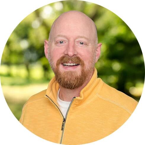 Counselor Scott Cable smiles in a bright yellow sweater in front of a nature background.