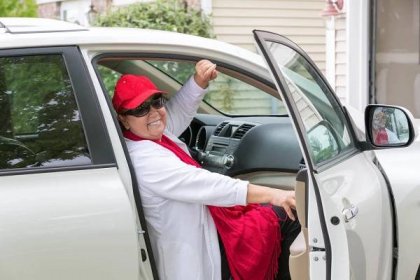 Seniorská dáma s červeným kloboukem sedí na sedadle spolujezdce připravena zavřít dveře a udeřit na silnici, má skutečný úsměv na tváři