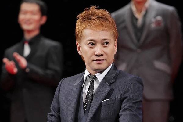 An Asian man with dyed red hair wearing a suit and a half smile.