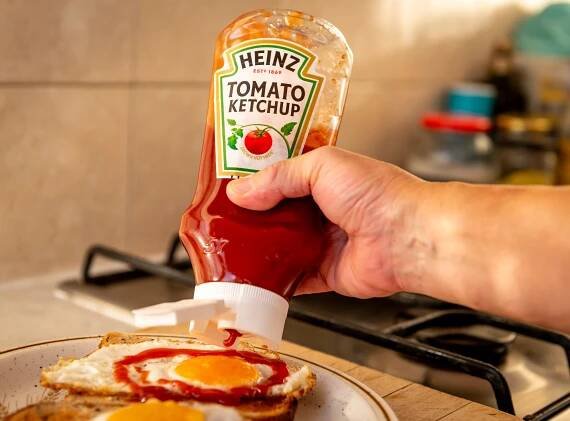 London. UK- 01.22.2023. A person squeezing a bottle of Heinz tomato ketchup on to fried eggs on toast. — Stock obrázek