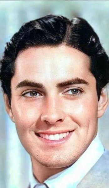 a close up of a person wearing a suit and tie smiling at the camera with a smile on his face