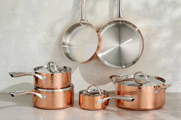 The BergHoff Vintage Copper Tri-Ply 10-Piece Hammered Cookware Set on a table and hung on hooks