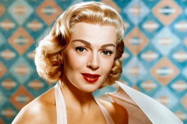 Lana Turner (1921-1995), US actress, wearing a sleeveless white dress and holding a white parasol in studio portrait, circa 1950.