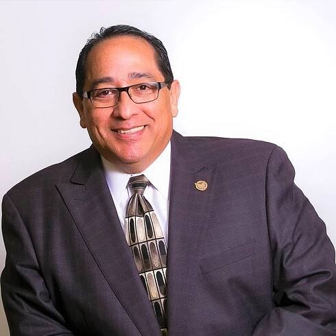 A man in a suit and tie smiling against a white background.