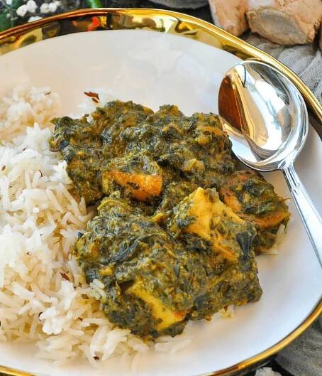 A white bowl consisting of jeera rice with palak paneer, and a silver spoon.