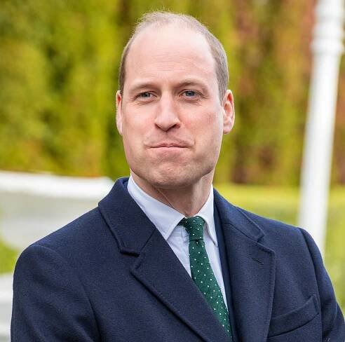 Prince William, Prince of Wales, in a dark blue suit and green tie.