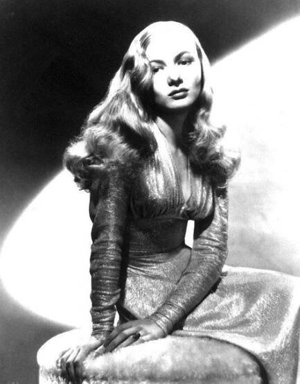 an old black and white photo of a woman sitting on a stool with her hair blowing in the wind