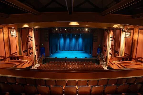 An empty auditorium with a stage and blue curtains.