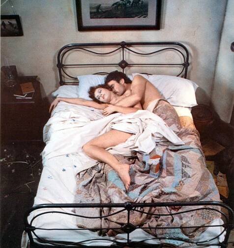 a man and a woman are laying on a bed under a quilt