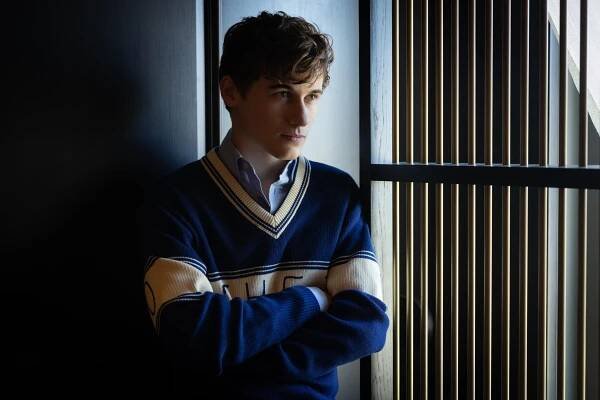 Sam Nivola stands, arms crossed, next to a window for a portrait.