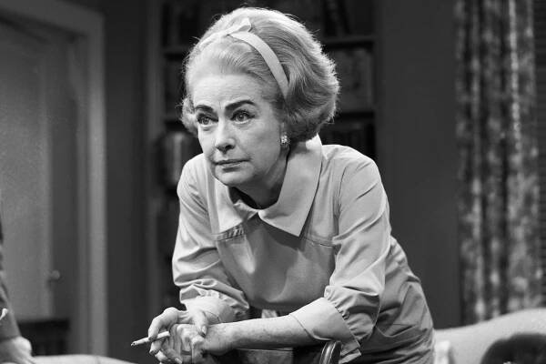 Joan Crawford leans over a chair in a black and white picture.