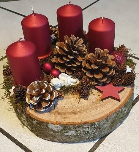 some red candles are sitting on top of a tree stump with pine cones and other decorations
