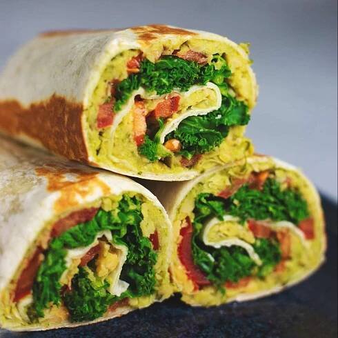 A tortilla wrap filled with chickpea, pesto, kale and tomato