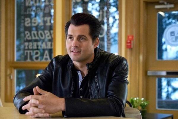 Kristoffer Polaha in a leather jacket sitting at the kitchen counter