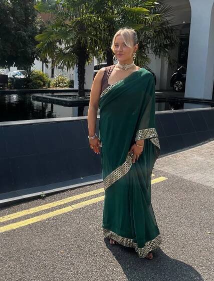 a woman in a green and gold sari stands in front of a building