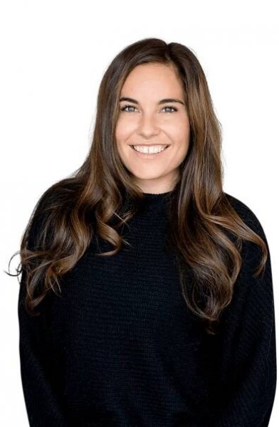 A woman with long hair is wearing a black sweater and smiling.