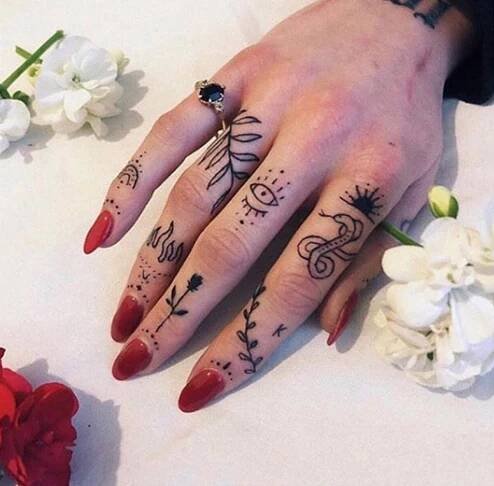a woman's hand with tattoos on it and flowers in the background next to her