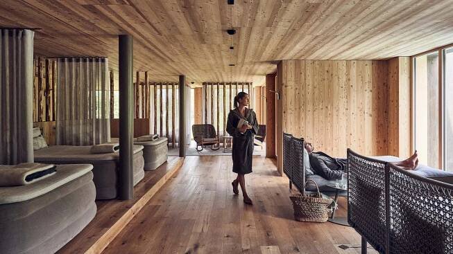 Frau in Bademantel in einer Spa-Lounge mit hölzernen Wänden und Böden, Liegen und einem liegenden Mann.