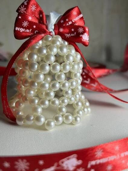 a bell shaped ornament is adorned with pearls and a red ribbon on a white surface