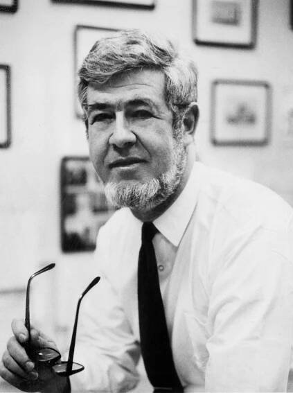 A black and white photo of Herbert J. Gans, with wavy hair and a beard, holding his glasses in his right hand.