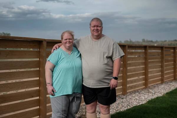 A couple stands together outside and the husband has his arm around his wife.