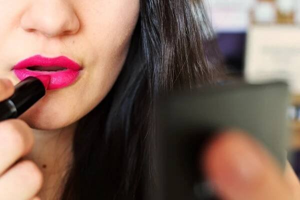 A woman puts on lipstick.