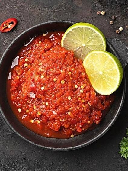 Homemade Sambal Oelek Chili Paste in a black bowl with slices of lime on top.