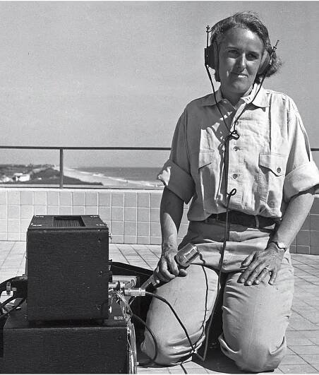 Barbara Lawrence kneeling outdoors in Florida, listening to dolphin vocalizations using headphones and equipment.