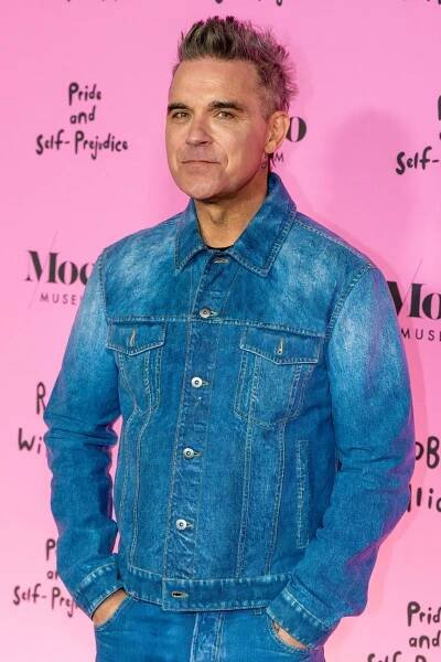 a man in a denim jacket stands in front of a pink wall that says pride and self-pride