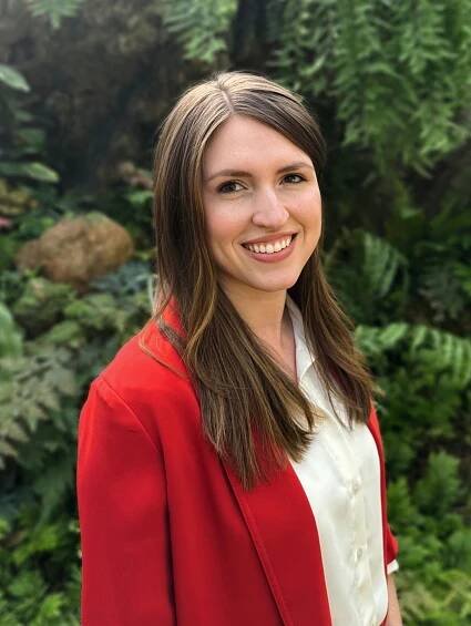 A portrait of Dr. Zoie Sheets smiling. A woman with brown hair a light complexion wearing a white shirt and red cardigan.