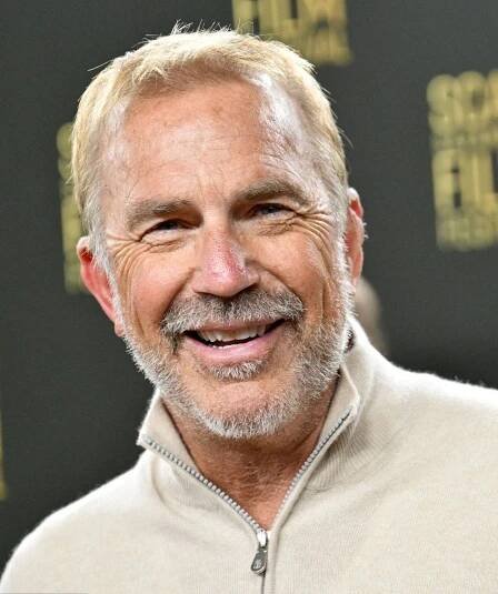 an older man smiling at the camera in front of a black backdrop with gold lettering