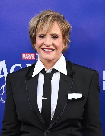 Patti LuPone in a stylish black suit with a white shirt and tie, smiling at a formal event