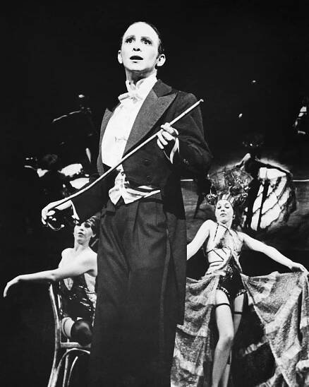 A black-and-white production image of a man in a tuxedo and holding a cane.