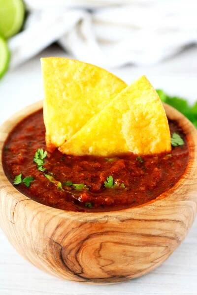 A small wood bowl with salsa inside of it and chip poking out of the top.
