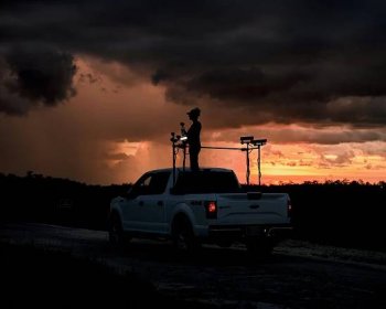 Amy Siewe stands in the back of her pickup truck, which is outfitted with spotlights, in the backdrop of sunset. 