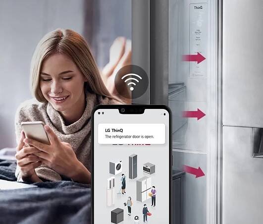 Smartphone ukazuje oznámení LG ThinQ o otevřených dveřích chladničky vedle kuchyňské scény.