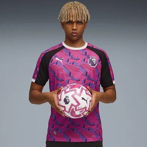 A model holding a football in front of a grey background wearing a patterned football shirt.