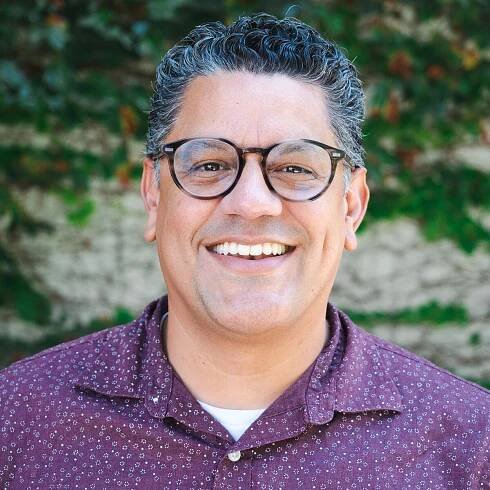 manny herrera smiling at camera wearing magenta button up shirt with small white designs