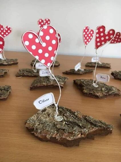 small red and white hearts on rocks with name tags attached to them, sitting on a wooden table