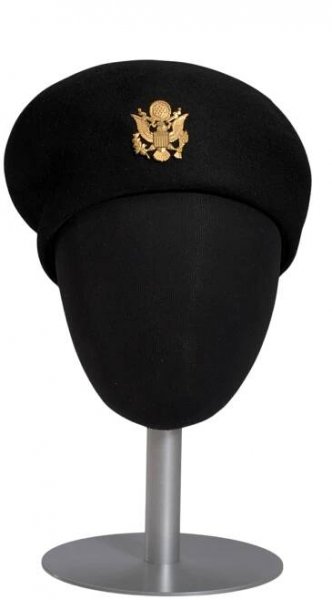Black US Army Nurse's dress uniform beret and insignia pin worn by Brigadier General Hazel Johnson-Brown. The black felt beret (a) is formed with a crease along the proper right side; the crease is deepest near the center back. The interior of the crown is lined in buckram and a black ribbon hat band. A US Army gold insignia pin (b) is attached with a double-pinback to the center front of the beret. An empty single hole with a metal grommet is on the beret below the pin.