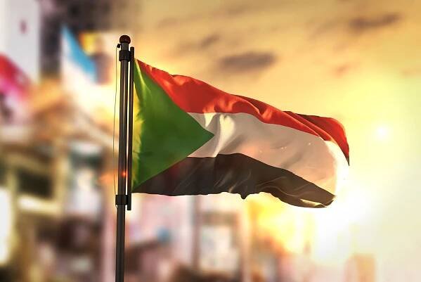 súdán vlajka proti městu rozmazané pozadí při východu slunce podsvícení - súdán východní afrika - stock snímky, obrázky a fotky